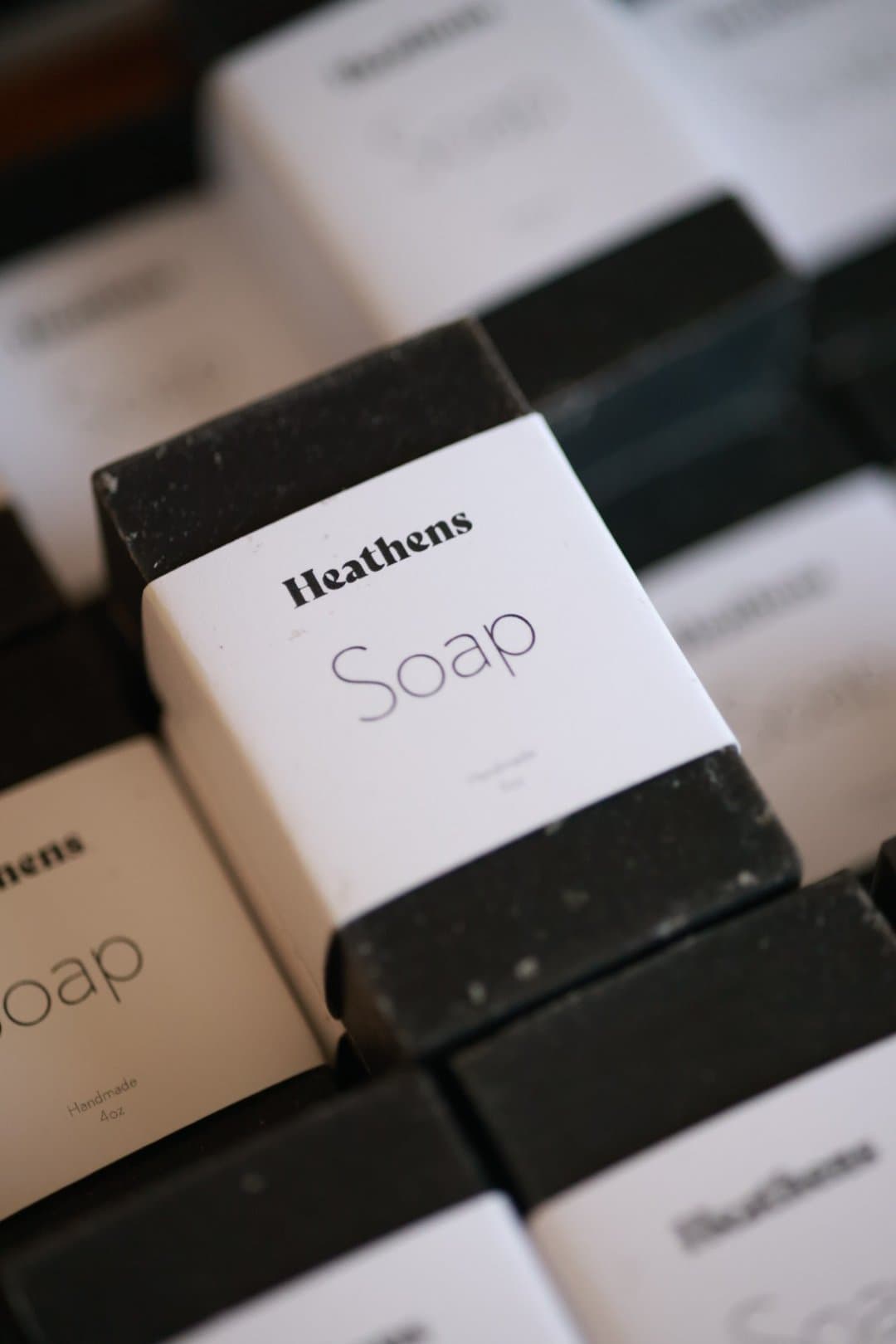 Bars of Heathens charcoal soap in their white paper wraps, laid out in rows.