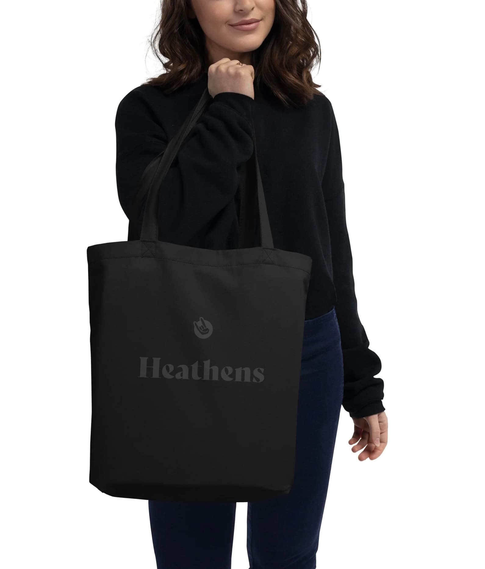 A woman carrying the black Heathens tote bag, printed with the icon and wordmark in dark gray.
